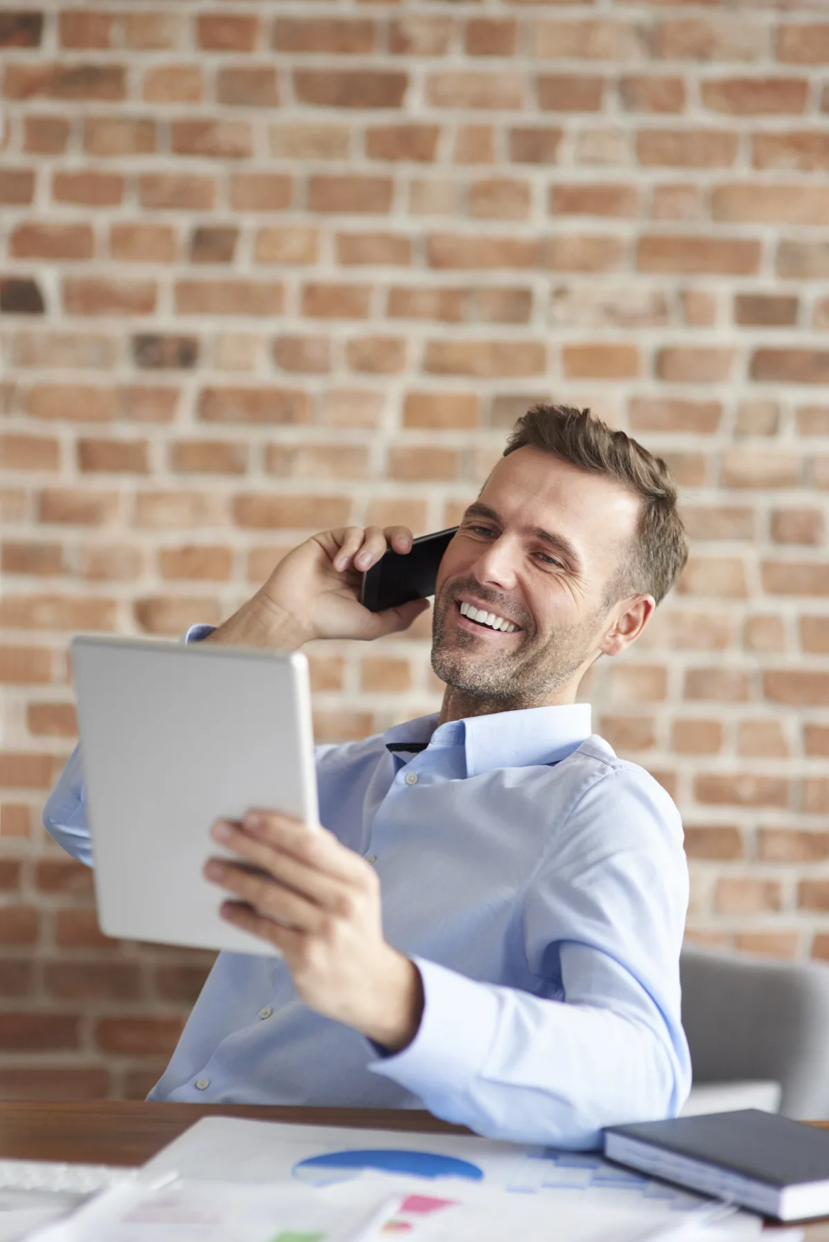 Directivo sonriente atendiendo una llamada mientras consulta informes en una tableta